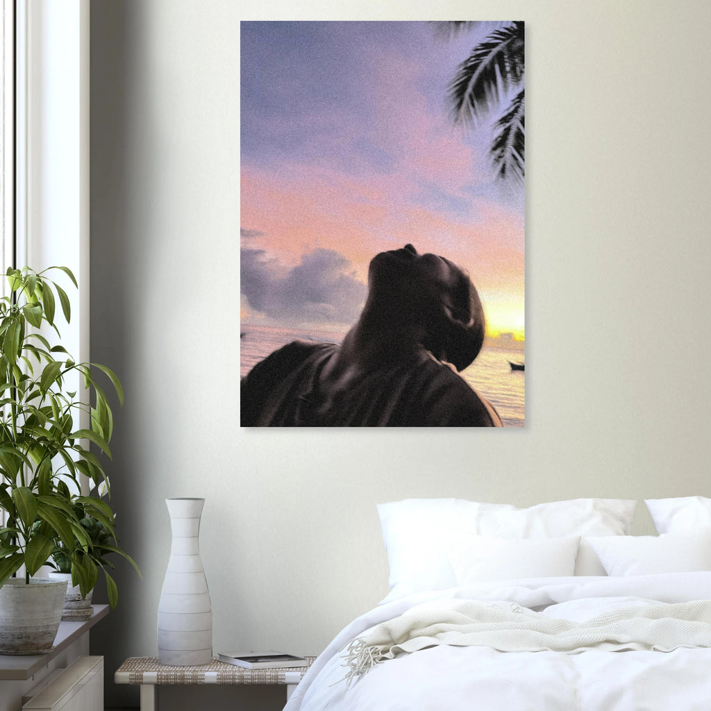 Artwork poster of a person looking at a sunset with palm trees on a wall above a bed.